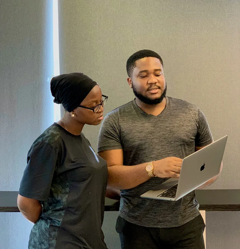 Two colleagues stand side by side, looking at a design on an open laptop.